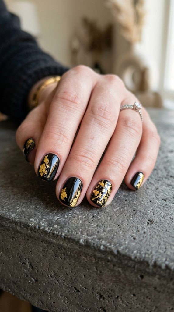 Sleek black fingernail design with gold foil accents