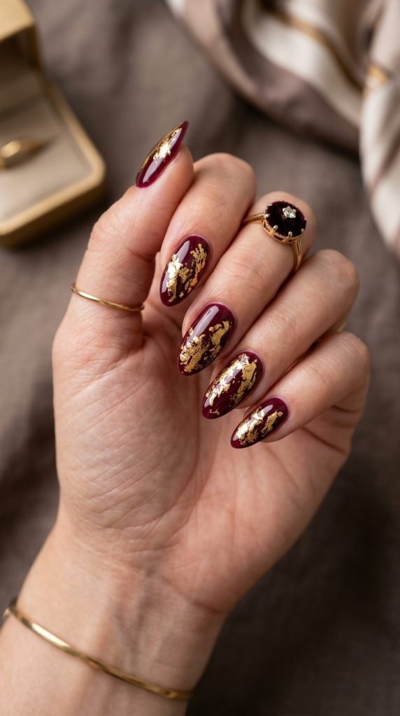 Burgundy dip nails with gold foil accents showing luxury two-tone design
