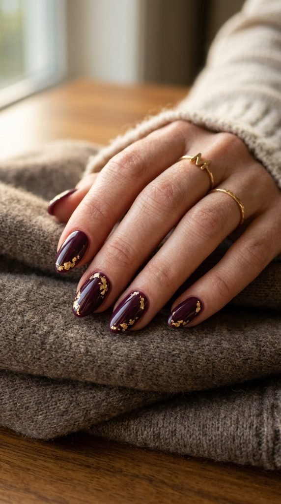 Deep plum gel nails with gold foil leaf botanical accents